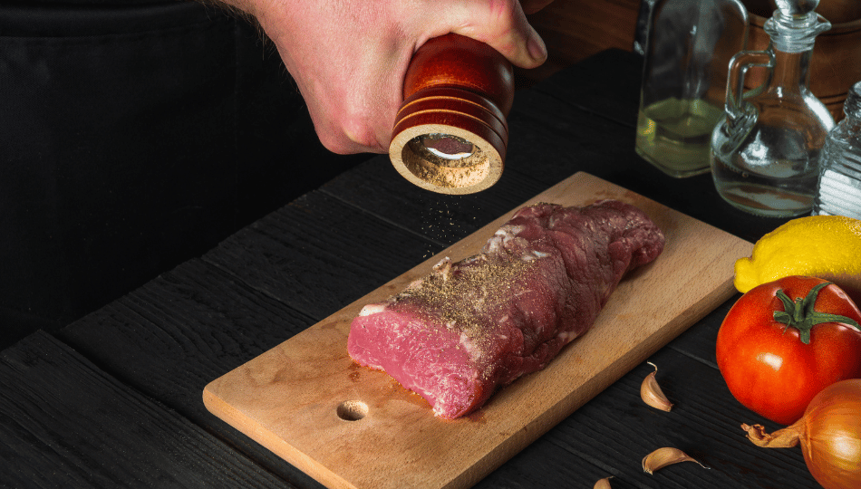 Frisches Rinderfilet wird auf einem Holzbrett mit einer Pfeffermühle gewürzt – Vorbereitung zum Raclette Fleisch Marinieren.
